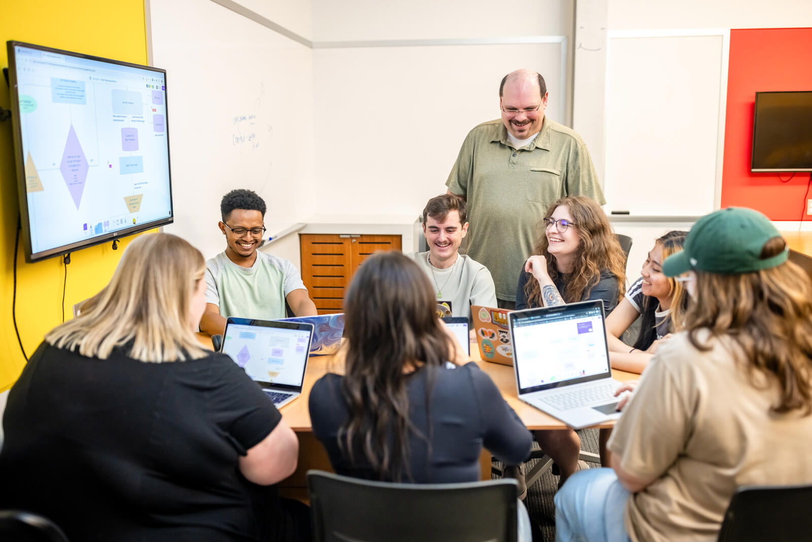 Dr. Daniel Pittman and a team of C3 Lab student researchers working on laptops around a table, with a project workflow diagram displayed on the screen behind them